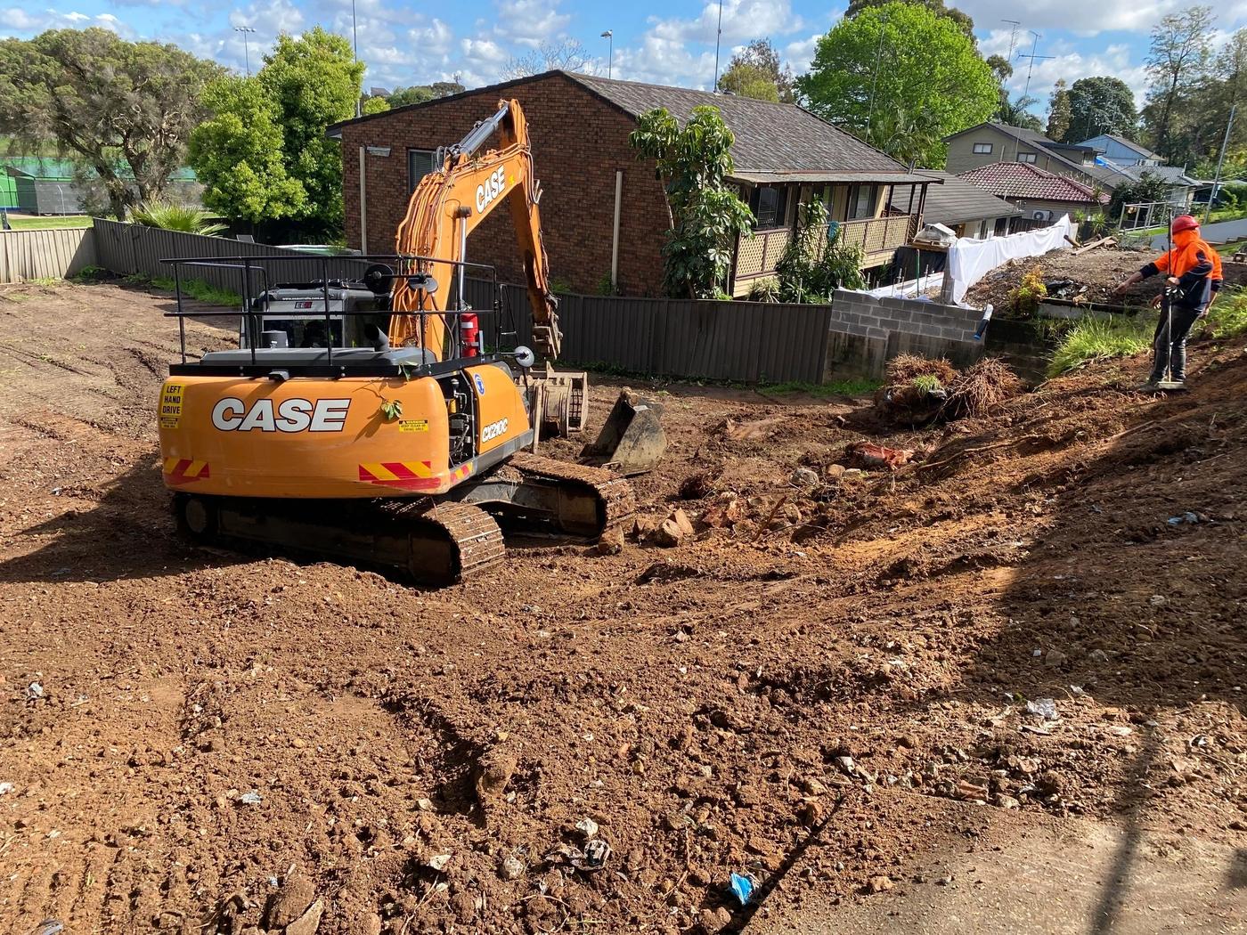 Excavator clearing a residential block with a worker in hi vis